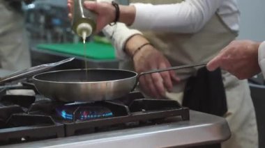 Ticari bir mutfakta çalışan profesyonel bir aşçı yemek pişirme tavaları ve diğer mutfak malzemelerinden yükselen buharlı bir yemek hazırlıyor.