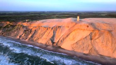 Tepenin tepesinde ünlü deniz feneri olan dev kum tepelerinin hava manzarası. Rubjerg Knude Deniz Feneri, Kuzey Deniz Rubjerg, Danimarka Lokken yakınlarındaki Rubjerg Knude Fyr deniz fenerinde gün batımı. 