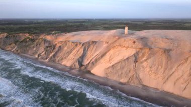 Tepenin tepesinde ünlü deniz feneri olan dev kum tepelerinin hava manzarası. Rubjerg Knude Deniz Feneri, Kuzey Deniz Rubjerg, Danimarka Lokken yakınlarındaki Rubjerg Knude Fyr deniz fenerinde gün batımı. 