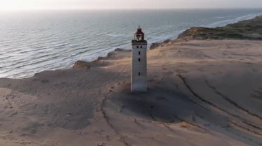 Tepenin tepesinde ünlü deniz feneri olan dev kum tepelerinin hava manzarası. Rubjerg Knude Deniz Feneri, Kuzey Deniz Rubjerg, Danimarka Lokken yakınlarındaki Rubjerg Knude Fyr deniz fenerinde gün batımı. 