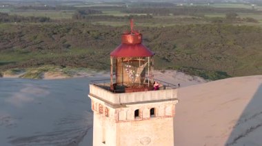 Tepenin tepesinde ünlü deniz feneri olan dev kum tepelerinin hava manzarası. Rubjerg Knude Deniz Feneri, Kuzey Deniz Rubjerg, Danimarka Lokken yakınlarındaki Rubjerg Knude Fyr deniz fenerinde gün batımı. 