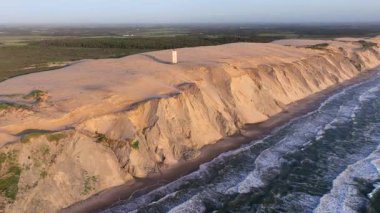 Tepenin tepesinde ünlü deniz feneri olan dev kum tepelerinin hava manzarası. Rubjerg Knude Deniz Feneri, Kuzey Deniz Rubjerg, Danimarka Lokken yakınlarındaki Rubjerg Knude Fyr deniz fenerinde gün batımı. 