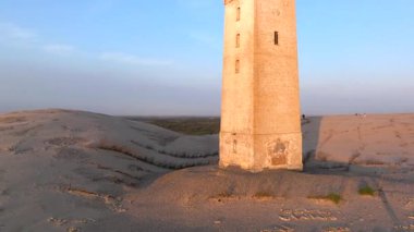 Tepenin tepesinde ünlü deniz feneri olan dev kum tepelerinin hava manzarası. Rubjerg Knude Deniz Feneri, Kuzey Deniz Rubjerg, Danimarka Lokken yakınlarındaki Rubjerg Knude Fyr deniz fenerinde gün batımı. 