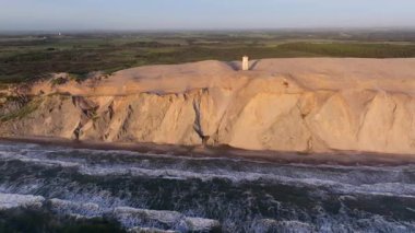 Tepenin tepesinde ünlü deniz feneri olan dev kum tepelerinin hava manzarası. Rubjerg Knude Deniz Feneri, Kuzey Deniz Rubjerg, Danimarka Lokken yakınlarındaki Rubjerg Knude Fyr deniz fenerinde gün batımı. 