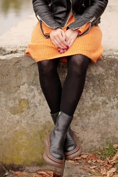 stock image woman sitting on the shore, female legs in a dress, female feet in boots