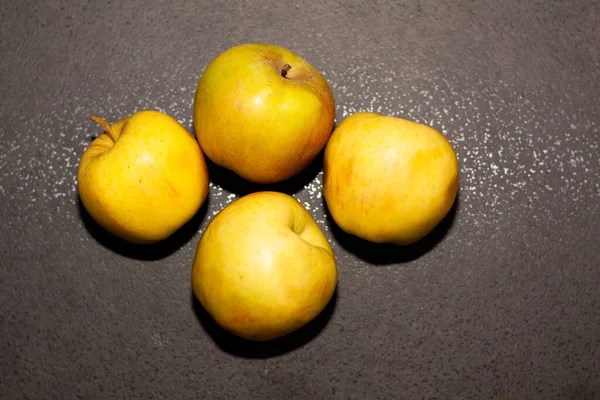 four yellow apples on a dark gray background