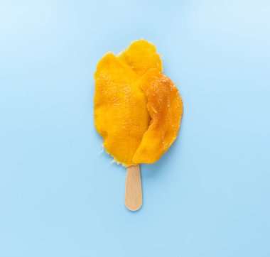 Dondurma çubuğunda kurutulmuş mango, mango dondurması, mavi arka plan.