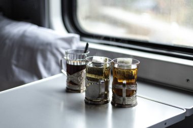 Pencerenin yanındaki tren kompartımanında masanın üzerinde üç bardak çay.