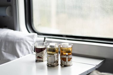 Pencerenin yanındaki tren kompartımanında masanın üzerinde üç bardak çay.