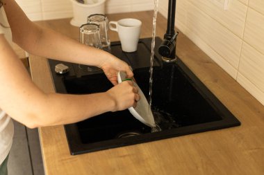 Kadın eli, genç bir kadın mutfaktaki lavaboda beyaz tabak yıkıyor, bulaşıkları yıkıyor.