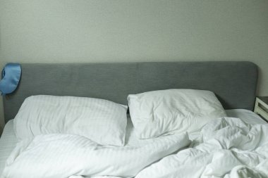 Yatak odası, beyaz çarşaflı yatak, yatağın arkasında mavi uyku maskesi, uyku konsepti.