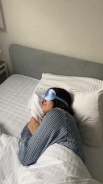 Genç bir kadın uyku maskesi takarak yatakta uyuyor.