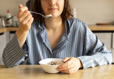 Genç bir kadın kahvaltıda yoğurtlu ve muzlu tahıl yer.