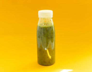 green smoothie drink in a transparent bottle on yellow background, healthy food