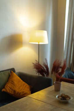 Kafede rahat bir köşe, turuncu yastıklı bir kanepe ve yer lambası.