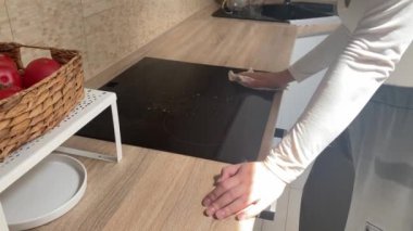 Evini temizleyen genç bir kadın mutfağı temizliyor, yemek pişirme yüzeyini paçavrayla siliyor.