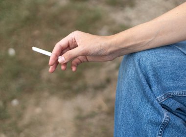 Kadının eli dizinde, elinde sigara tutuyor.