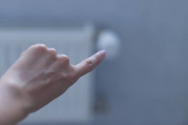 Kadın parmağıyla batarya ısıtma düğmesini işaret ediyor. Evde, bir dairede ısıtma. Isıtma fiyatları