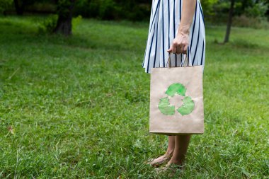 Genç bir kadın elinde yeşil bir çimenliğin arka planında bir eko-paket tutuyor.