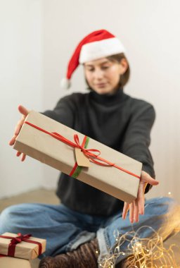 Noel Baba şapkalı genç bir kadın Noel hediyesi veriyor.