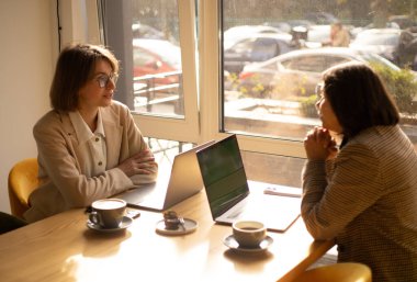 Cowork, iki kadın iş yerinde laptoplarla konuşuyor.