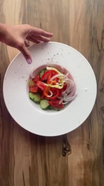 Kadın eli masanın üzerinde taze salatalık, domates, zeytinyağlı soğan salatası ile bir tabak tutuyor.