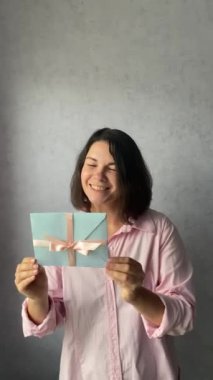 Genç bir kadın elinde pembe kurdeleli bir hediye çeki tutuyor.