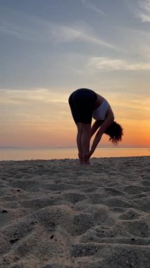 Sahilde bir kız yoga yapıyor. Güneşi selamlıyor.