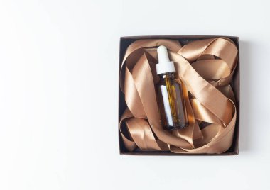 Beyaz bir zemin üzerinde serum şişesi olan bir kutu. Kurdeleli mocha mus rengi.