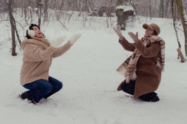 İki kadın bir kış ormanında kartopu atıp köpekle yürüyüşe çıkıyor.