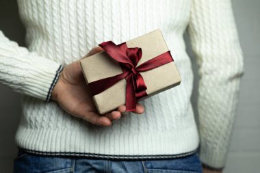 Adam arkasında bordo saten bir kurdele olan bir hediye saklıyor.