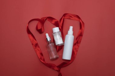 cosmetic face serum, enzyme face wash powder and cosmetic face spray in abstract red heart from red satin ribbon, love concept