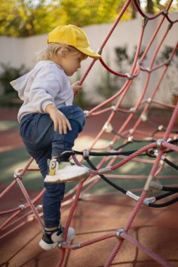 Üç yaşında bir çocuk oyun parkında iple oynuyor.