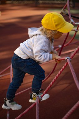 Üç yaşında bir çocuk oyun parkında ipe tırmanıyor.