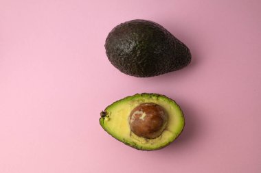 Pembe arka planda yarım ve tüm avokado.