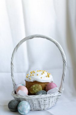 Beyaz kremalı Paskalya pastası ve beyaz hasır sepetli Paskalya yumurtaları.