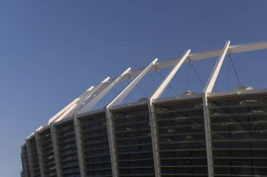 Güneş tarafından aydınlatılan bir spor stadyumunun yapısal unsurları mavi gökyüzü arka planına karşı