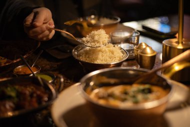 Hint yemeği tavuk körisi, arka planda bir adamın eli kaşıkla pirinç döküyor.