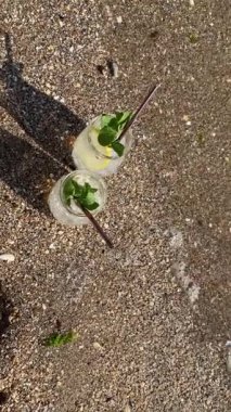 Üst manzara, deniz kıyısında limon ve nane yapraklı iki kokteyl.