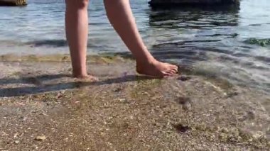 Bir kadın deniz kıyısında yürüyor, kadın bacakları suda.