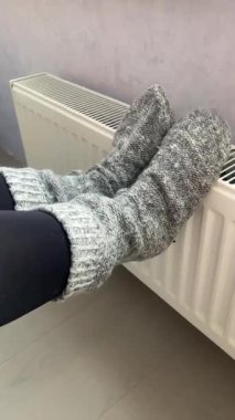 Örgü çoraplı kadın bacakları bir batarya, akü ısıtma düğmesi, bir dairede ısıtma.