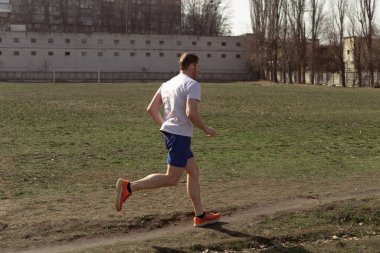 Yazın şehirde beyaz tişört ve mavi şort giyen profesyonel bir koşucu koşuyor.