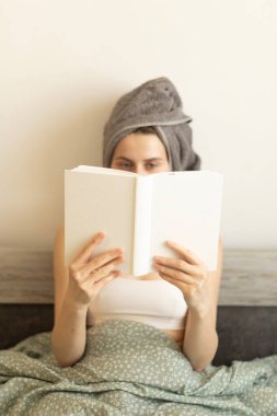 Kafasında havluyla yatakta kitap okuyan bir kadın.
