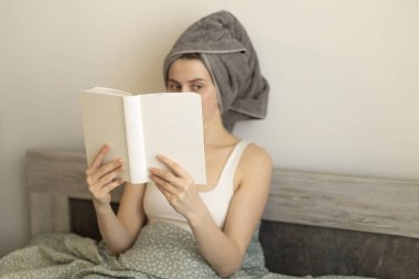 Kitaplı kadın yatakta oturuyor.
