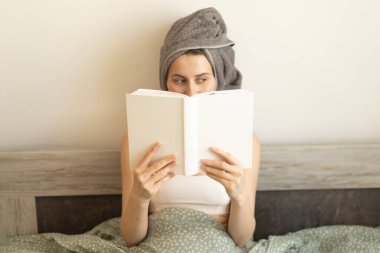Kafasında havluyla yatakta kitap okuyan bir kadın.