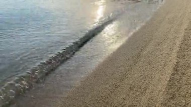 Sakin bir deniz dalgası güneş tarafından aydınlatılır ve kumlu bir kıyıda, dinlenme konseptinde batar.