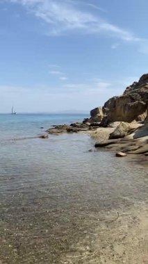 Kayanın yanındaki açık deniz suyu, ufuktaki yelkenli.