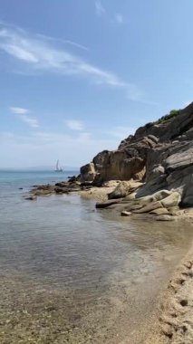 Kayanın yanındaki açık deniz suyu, ufuktaki yelkenli.