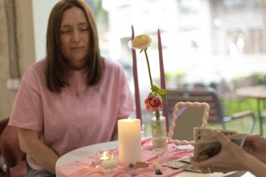 Tarot okuma oturumunda sakin bir an: müşteri ve tarot okuyucu, mistik ambiyansla dolu, pembe renkli rahat bir masaya bağlanır.