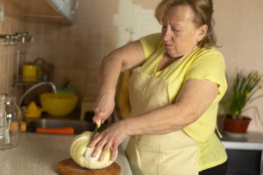 Önlük giymiş olgun bir kadın mutfağında ev yapımı lahana turşusu için salamura hazırlıyor. 